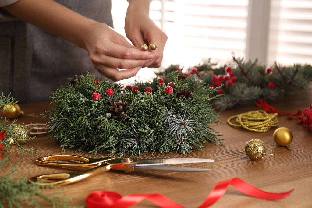Florist macht schönen Weihnachtskranz an Holztisch drinnen, Nahaufnahme - Foto, Bild