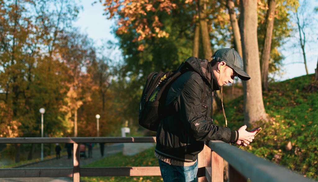 Ένας νεαρός με σακίδιο ενώ ταξιδεύει στο πάρκο ακούγοντας μουσική. - Φωτογραφία, εικόνα