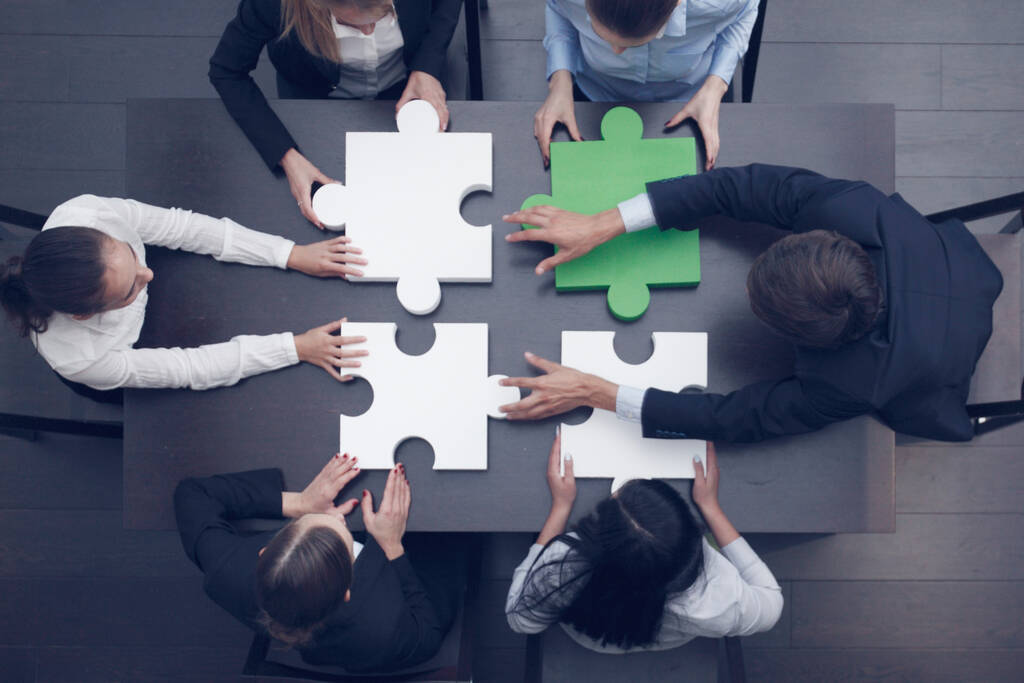 Группа деловых людей, собирающих головоломку за столом офиса, вид сверху, командная поддержка и концепция помощи, зеленые и белые части - Фото, изображение