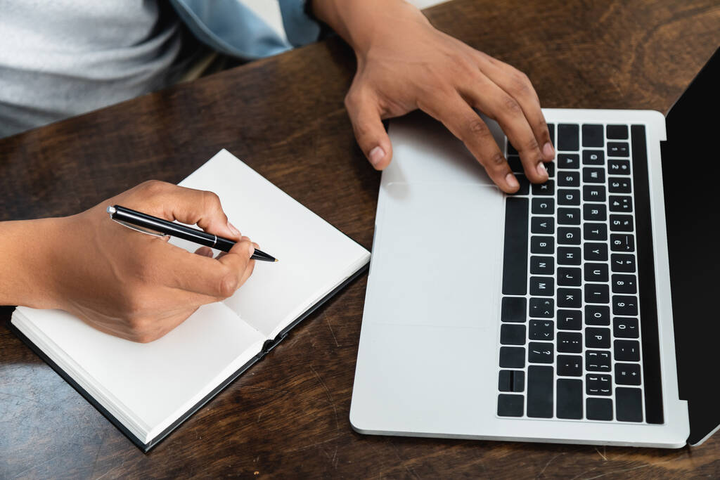 обрізаний вид на афроамериканця, який тримає ручку біля ноутбука і використовує ноутбук
 - Фото, зображення