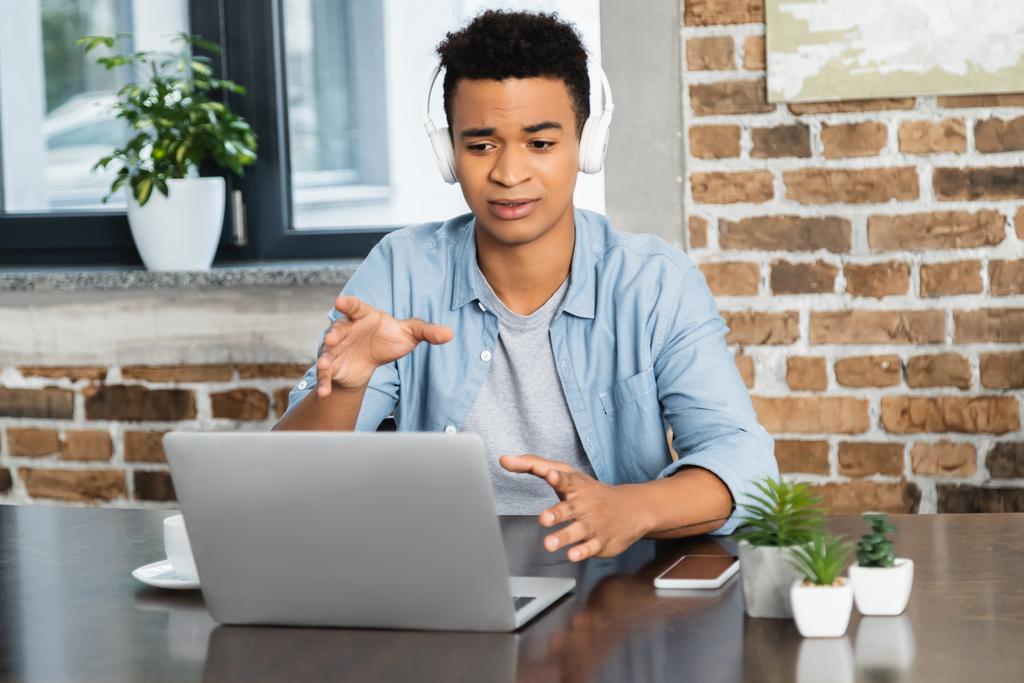アフリカ系アメリカ人の男性が机の上のノートパソコンの近くでポッドキャストを聞いて - 写真・画像