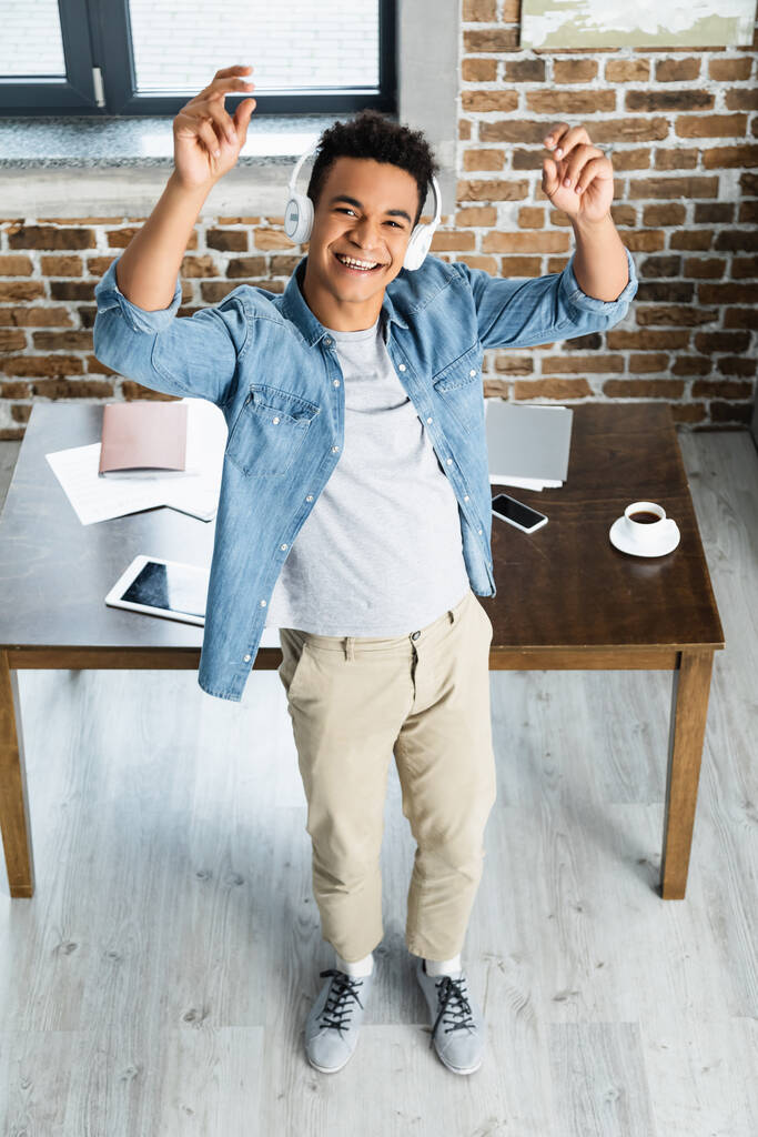 vue grand angle de heureux homme afro-américain debout près du bureau avec des gadgets - Photo, image