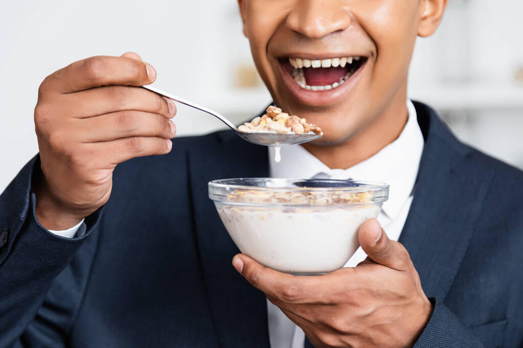 gewas uitzicht van verbaasd Afrikaans-Amerikaanse zakenman holding bowl met cornflakes en melk  - Foto, afbeelding
