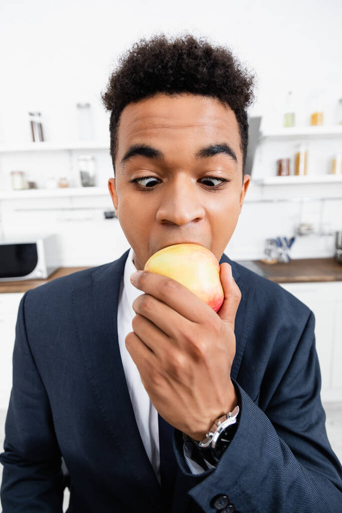 hombre de negocios afroamericano rizado comiendo manzana fresca en casa - Foto, imagen
