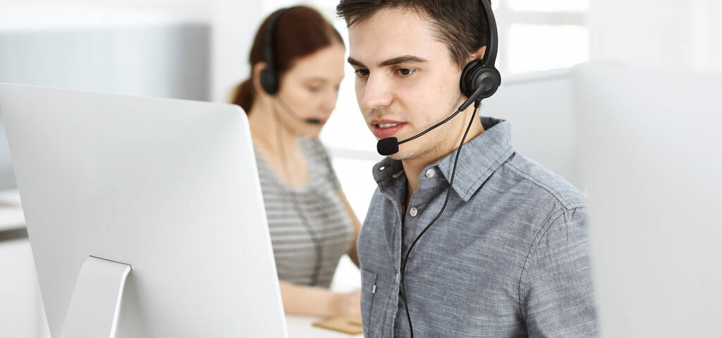 İnternette müşterilerle konuşurken kulaklık ve bilgisayar kullanan sıradan giyinmiş genç bir adam. Bir grup operatör iş başında. Çağrı merkezi - Fotoğraf, Görsel