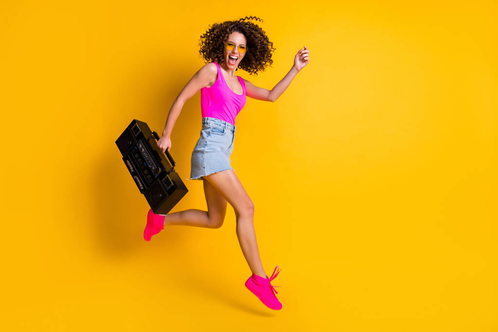 面白い巻きヒップスターdj女性のフルボディ写真ホールドレトロテープブームボックス急いでイベント休日ジャンプ来るビーチウェア日仕様ピンクシングルデニムスカートシューズ隔離された黄色の色の背景 - 写真・画像