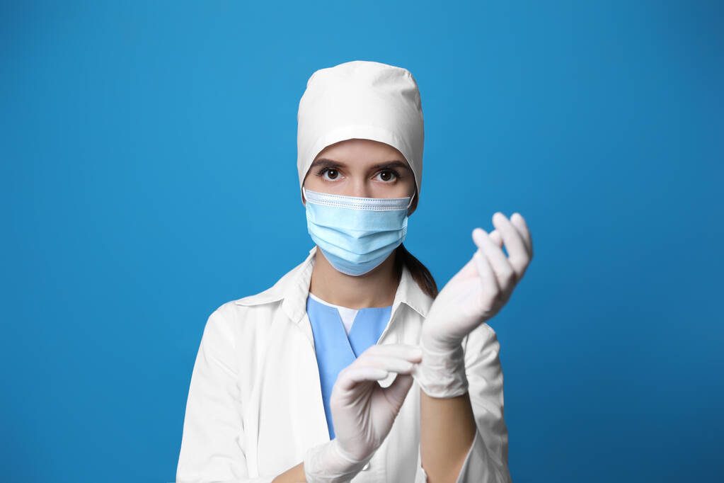 Lääkäri suojaava naamio laittaa lääketieteelliset käsineet vastaan sininen tausta - Valokuva, kuva