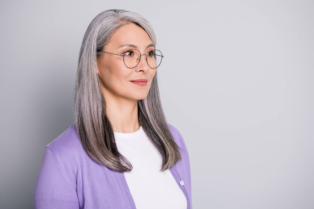 Foto de retrato de una mujer de negocios mayor con experiencia concentrada y confiada que usa anteojos y cárdigan púrpura aislados en un fondo de color gris - Foto, imagen