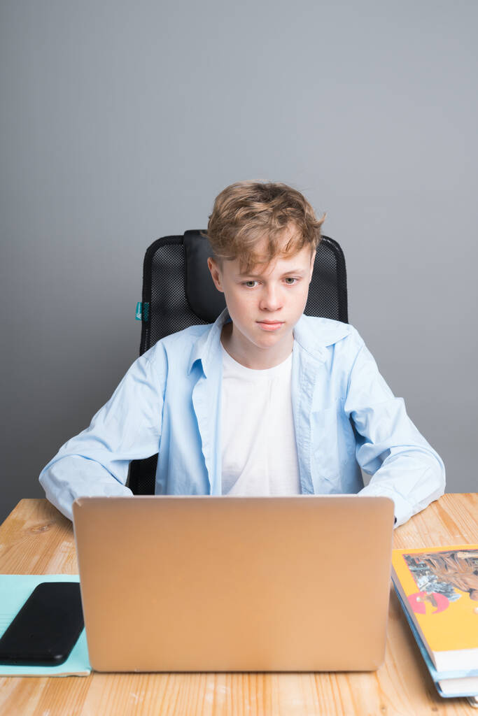 Un giovane studente in camicia blu siede a una lezione online, a un tavolo in attesa dell'inizio della lezione al computer. Istruzione durante la pandemia di coronavirus - Foto, immagini