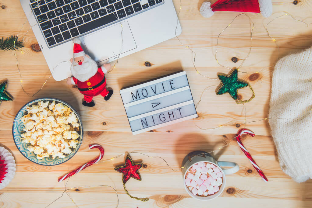 Top view Christmas Movie night concept. Flat lay composition with Movie night message on the board, laptop, popcorn bowl, decor, a cup of cocoa with marshmallows and warm plaid on wooden background. - Photo, Image