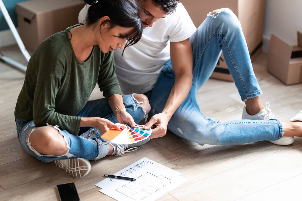 Молодая привлекательная пара, сидя на полу, выбирает цвета в цветовой палитре для окраски стен квартиры. - Фото, изображение