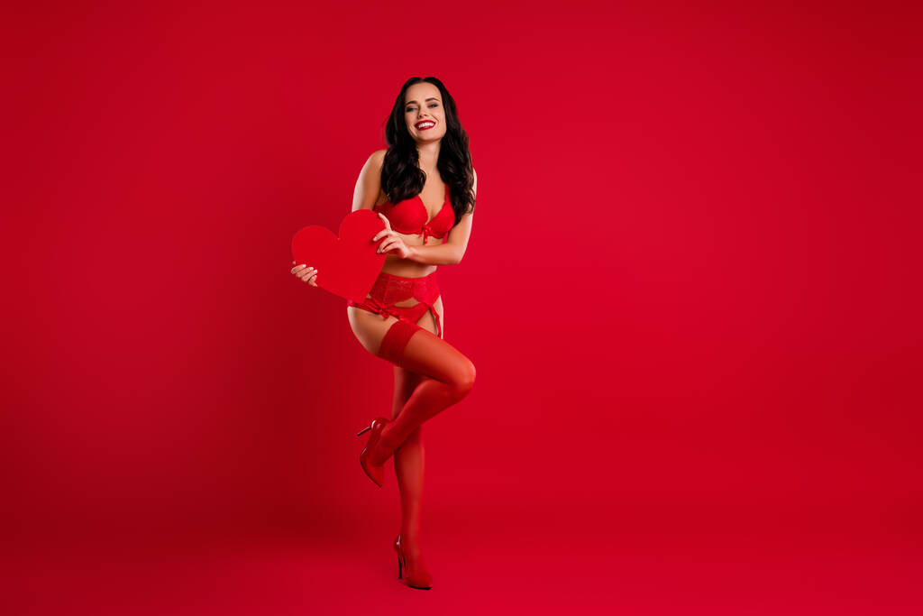 Foto de corpo inteiro de mulher de cabelos castanhos deslumbrante alegre segurar estilete desgaste do coração isolado no fundo de cor vermelha - Foto, Imagem
