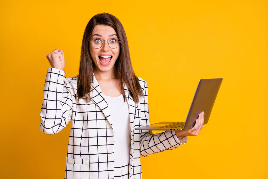 Foto retrato de mulher surpreendida trabalhando no computador gesticulando como vencedor isolado no fundo cor amarela vibrante - Foto, Imagem