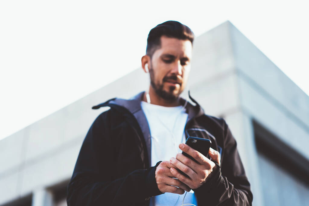 現代のスマートフォン技術上の4gインターネット接続を使用してメディアアプリケーションのための通知を確認ヘッドフォンで白人男性のぼやけたビューの下で、男性ブロガーは受信SMSメッセージを読み取ります - 写真・画像