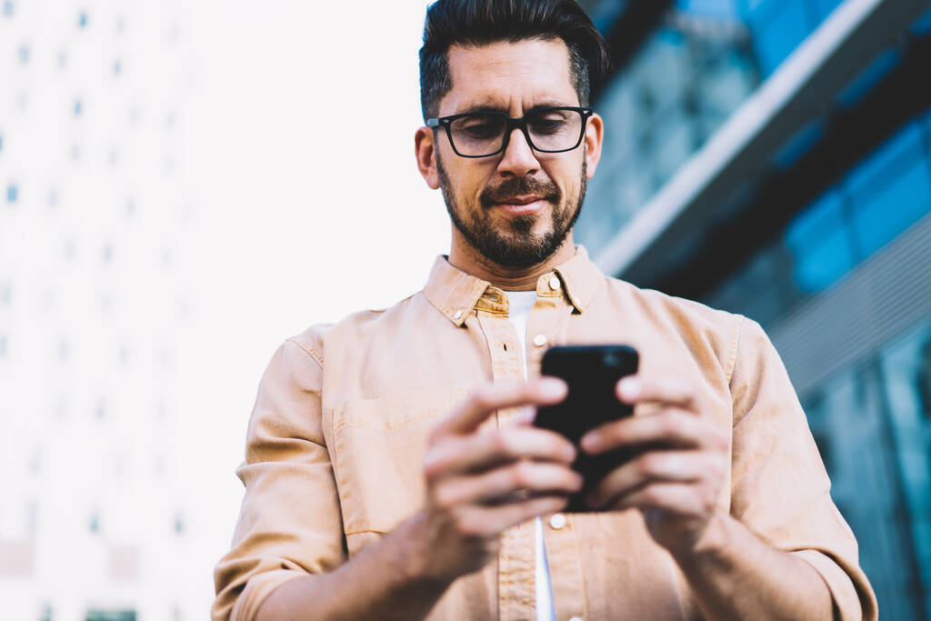 Gözlük takan beyaz erkek blog yazarı, akıllı telefon aygıtı ve açık havada 4G internet kullanarak e-posta mesajı yazıyor, cep telefonuyla sosyal ağda erkek gözlüğü okuyor. - Fotoğraf, Görsel