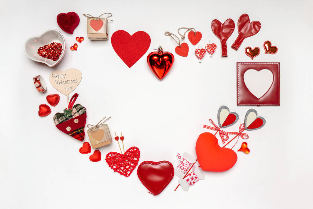 さまざまな装飾的な赤いハートとロマンチックなアイテムで作られたハートシンボル:ギフト、お菓子、白い背景のフォトフレーム。愛、ロマンス、バレンタインデーのコンセプト。テキスト用スペース付きグリーティングカード. - 写真・画像