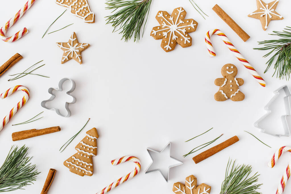 クリスマス、冬、新年の組成。白い背景にモミの木の枝、シナモンスティック、キャンディー、ジンジャーブレッドで作られたクリスマスフレーム。フラットレイアウト、トップビュー、コピースペース - 写真・画像