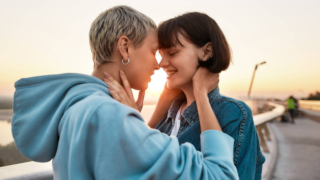 Zwei Frauen lächeln vor dem Kuss, junges lesbisches Paar genießt romantische Momente zusammen bei Sonnenaufgang - Foto, Bild