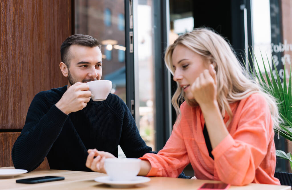 Giovane coppia caucasica innamorata che comunica nel tempo libero discutendo idee e bevendo caffè al caffè, colleghi uomini e donne degli anni '20 che conversano amichevolmente in pausa - Foto, immagini
