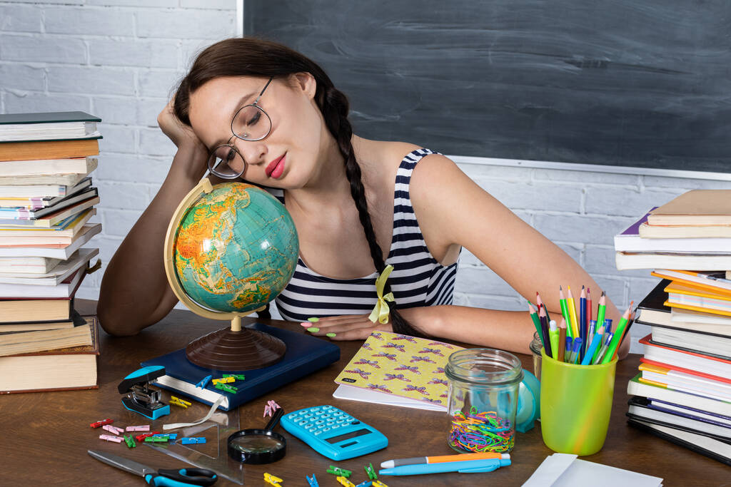 Durante una lección de geografía, una adolescente observa el mundo y planea tranquilamente sus viajes de verano. Una joven con gafas se sienta en un escritorio de la escuela. - Foto, imagen