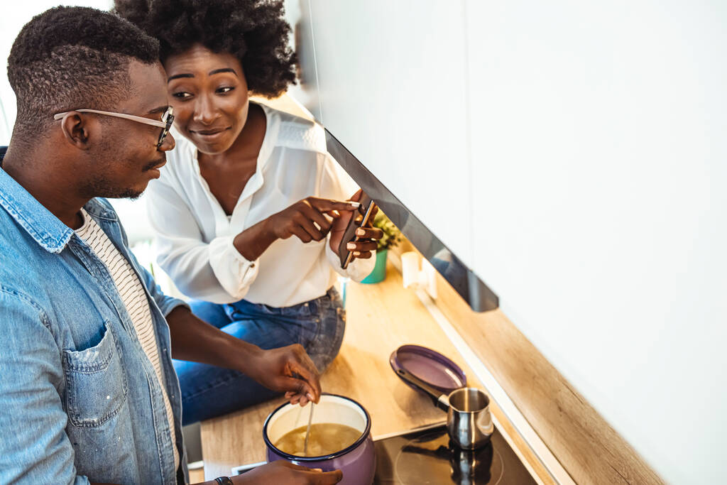 Kuvattu onnellisesta nuoresta pariskunnasta älypuhelimella valmistettaessa terveellistä ateriaa yhdessä kotona. Pari surffailu net kosketuslevy kun ruoanlaitto keittiössä. - Valokuva, kuva