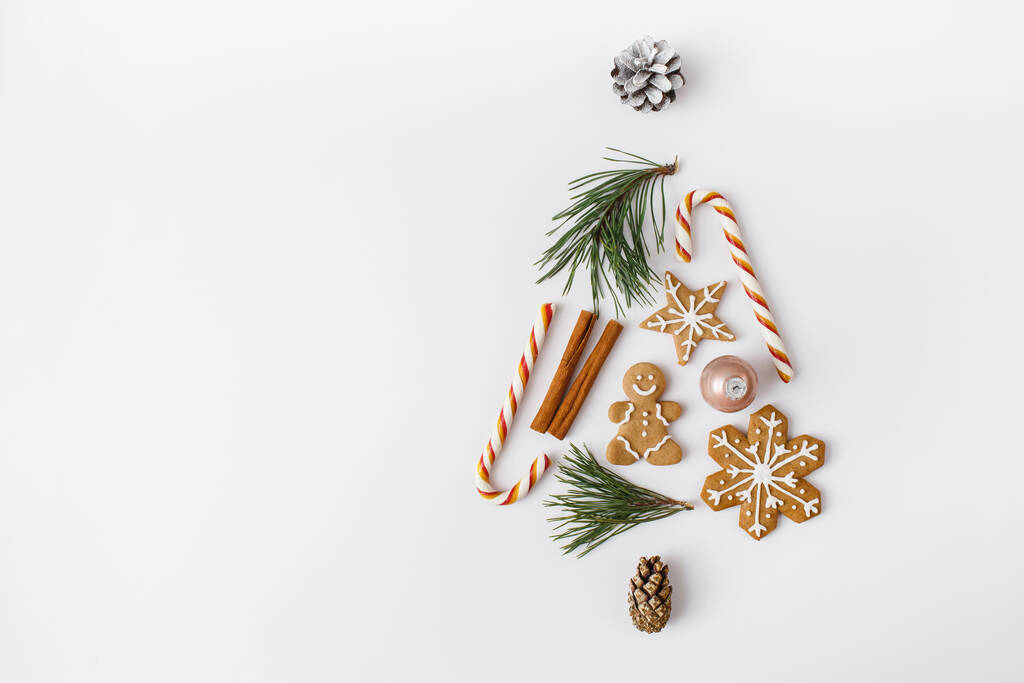 Noël, hiver, composition du nouvel an. sapin créatif fait de branches de sapin, cône de pin, bâtons de cannelle, bonbons, pain d'épice sur fond blanc. Pose plate, vue du dessus, espace de copie - Photo, image