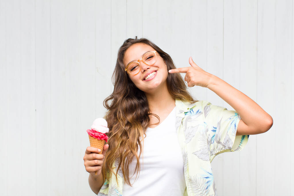 junge hispanische Frau lächelt selbstbewusst und zeigt auf ihr eigenes breites Lächeln, positive, entspannte, zufriedene Haltung - Foto, Bild