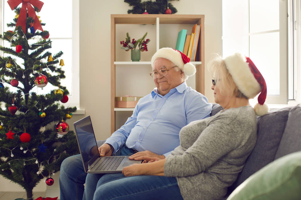 Mutlu yaşlı çiftin dizüstü bilgisayar kullanarak favori Noel filmlerini izlemesinin yan görüntüsü. - Fotoğraf, Görsel