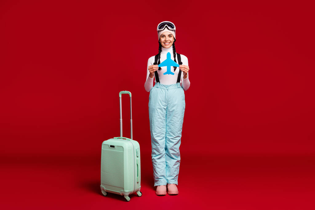 Pełnowymiarowe zdjęcie młodej pięknej pozytywnej dziewczyny z ogonami i niebieskimi spodniami trzymać karty papieru samolot izolowane na czerwonym tle - Zdjęcie, obraz