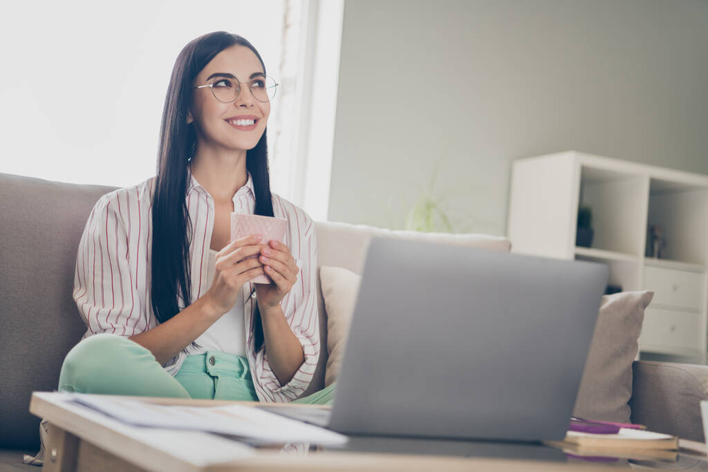 夢のような陽気な若い女性の肖像写真は、ノートパソコンの笑顔の近くに座って自宅からリモートで働くコーヒーのカップを維持 - 写真・画像