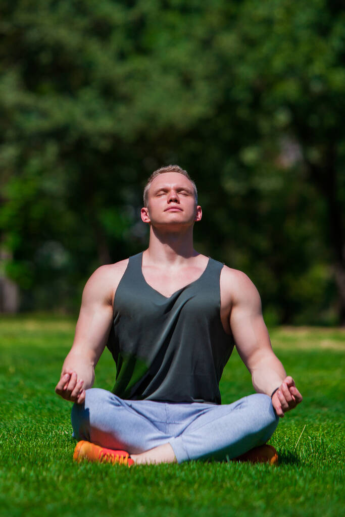 Jeune homme musclé fait du yoga dans un parc d'été. Homme sportif est assis dans la position Lotus et se détendre à l'extérieur - Photo, image