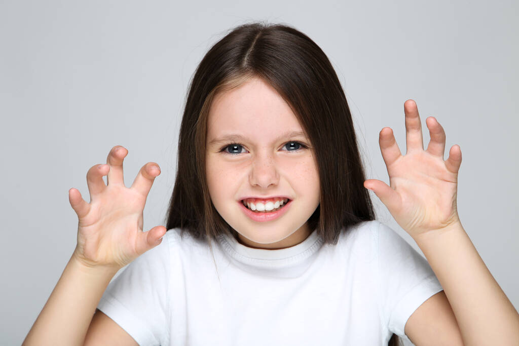 Молода дівчина показує кігті жестів руками на сірому фоні
 - Фото, зображення