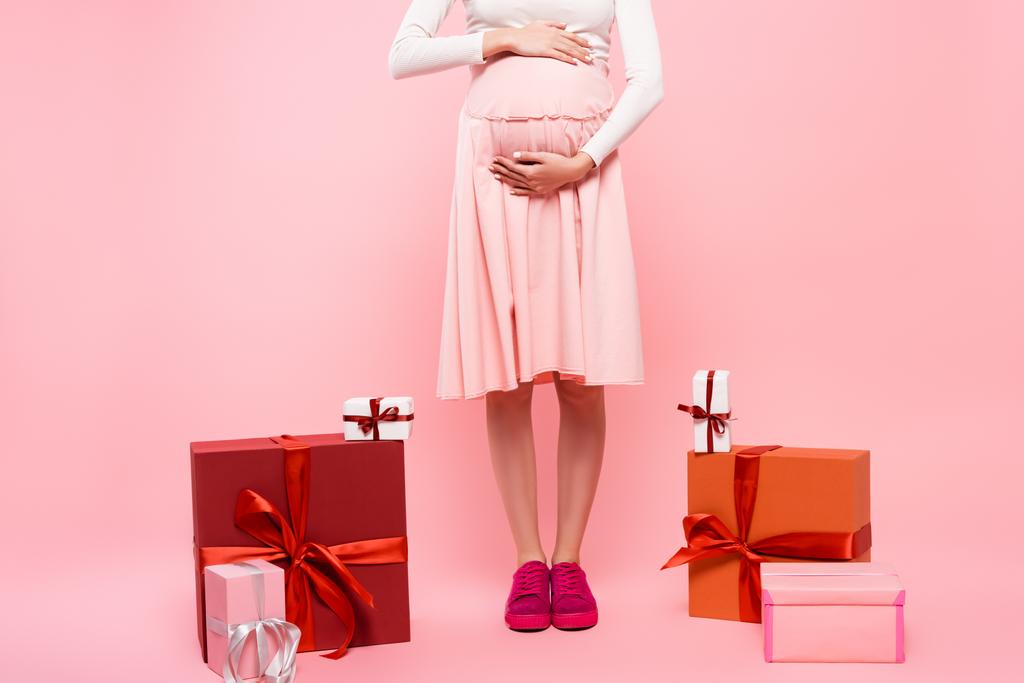 vista cortada de jovem mulher grávida bonita com presentes isolados em rosa - Foto, Imagem