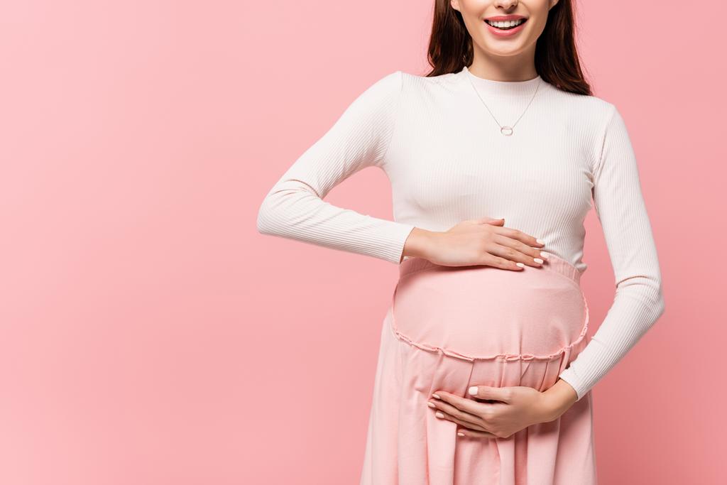 περικοπή άποψη της ευτυχούς νεαρή όμορφη έγκυος γυναίκα αγγίζοντας την κοιλιά απομονώνονται σε ροζ - Φωτογραφία, εικόνα