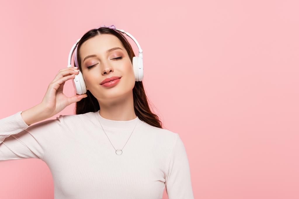 glückliche junge hübsche Frau mit Kopfhörer, die Bauch isoliert auf rosa berührt - Foto, Bild