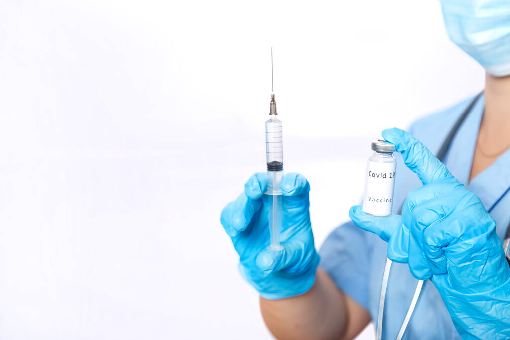 マスクされた医者の手の中にコロナウイルスワクチンと注射器を持つバイアル。横写真. - 写真・画像