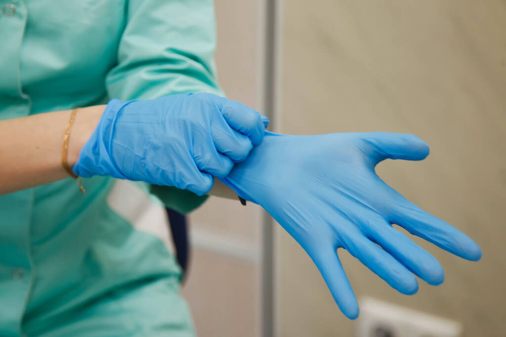 Doctor in dressing gown puts on sterile blue gloves. Concept of hero of doctors and stress. Concept of infection control. Risk of infection spreading. Copy space - Photo, Image