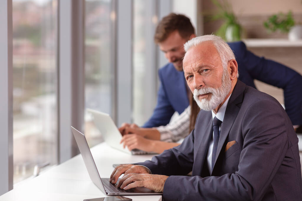 Senior menedzser használ egy laptop fiatal kollégák a háttérben - Fotó, kép
