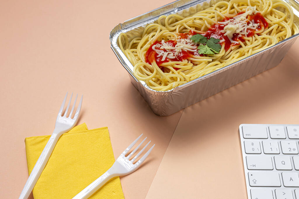 İş yerinde öğle yemeği ve bilgisayar klavyeli domates ve peynirli sağlıklı spagetti. Ofis konsepti için ev yemeği. Yemeği götür. - Fotoğraf, Görsel