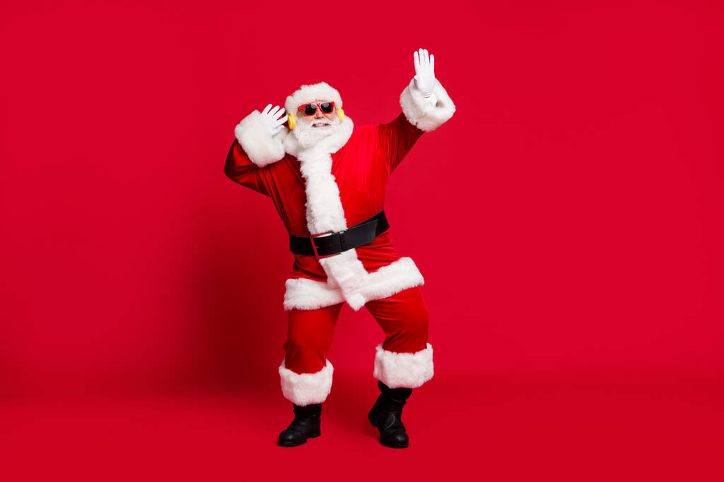 Full length photo of pensioner old man grey beard dancing carefree wear santa costume gloves coat belt sunglass headwear wireless earphones black leather boots isolated red color background - Photo, Image