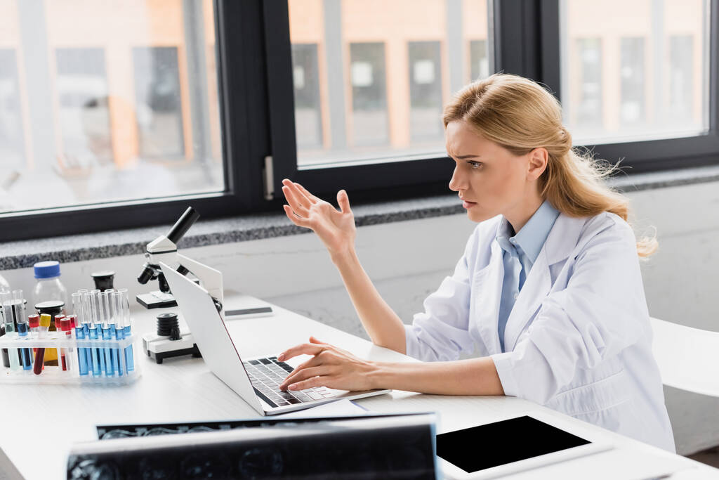 displeased scientist gesturing near laptop and microscope in lab - Photo, Image