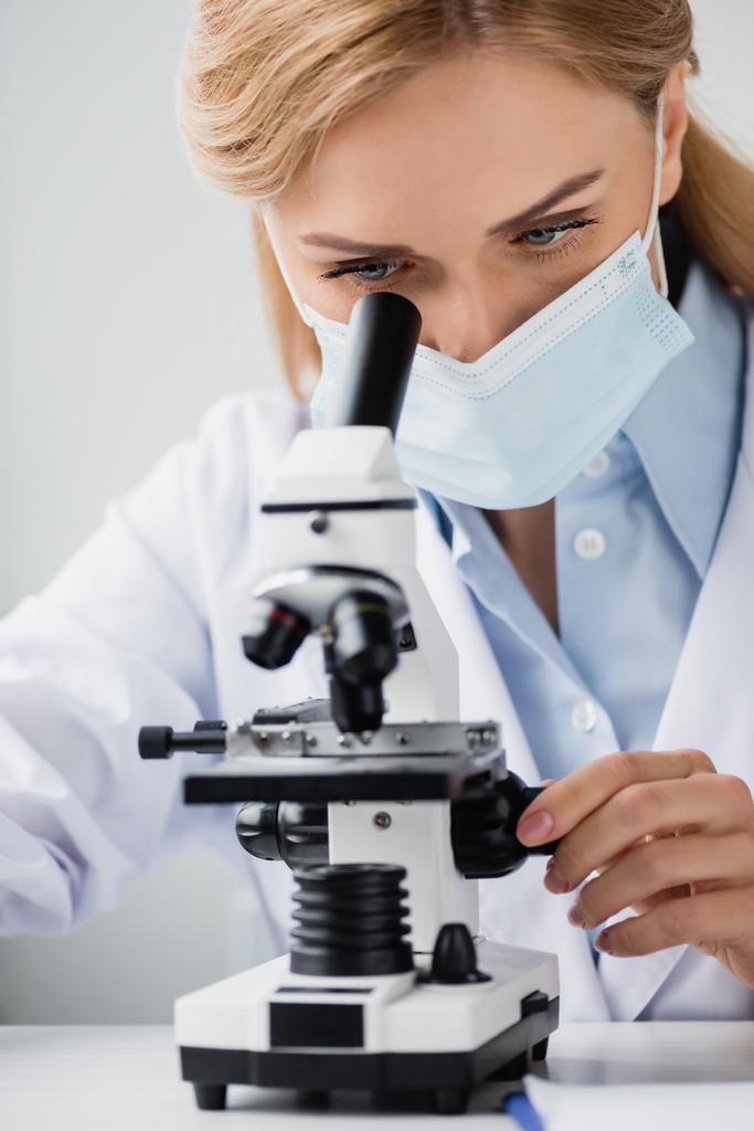 женщина-ученый в медицинской маске смотрит в микроскоп в лаборатории  - Фото, изображение