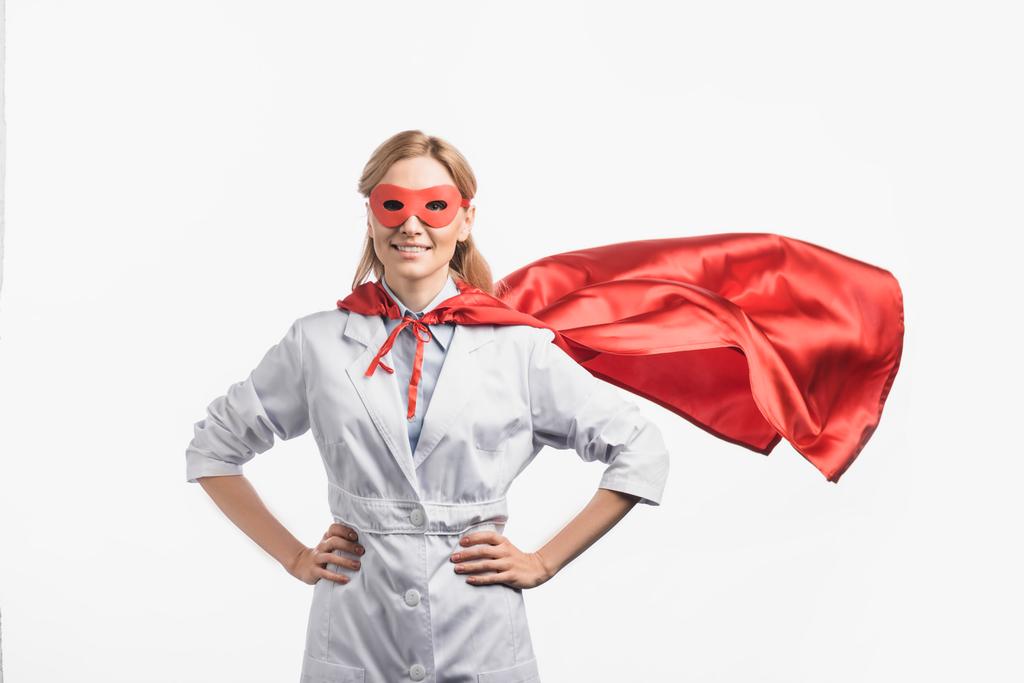 enfermeira feliz em máscara de super-herói e capa de pé com as mãos em quadris isolados em branco - Foto, Imagem