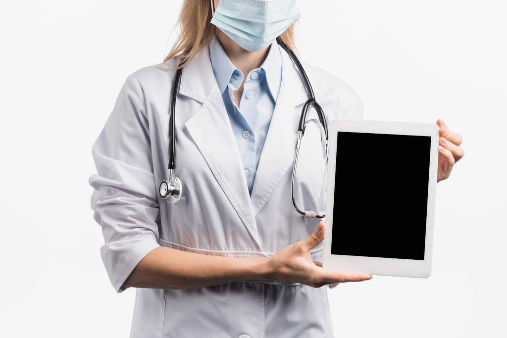 vágott kilátás ápoló orvosi maszk és fehér kabátot tartó digitális tabletta üres képernyő elszigetelt fehér  - Fotó, kép
