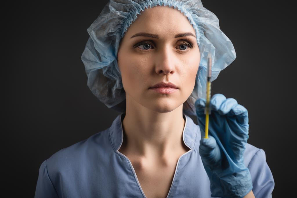 Spritze mit Impfstoff in der Hand einer Krankenschwester in Latex-Handschuh auf verschwommenem Hintergrund isoliert auf dunkelgrau - Foto, Bild