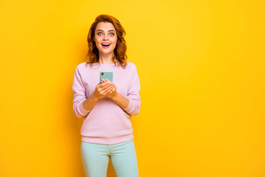 Foto van grappige gekke dame houden telefoon moderne technologie lezen positieve reacties populaire blog dragen roze pullover groene broek geïsoleerde gele kleur achtergrond - Foto, afbeelding