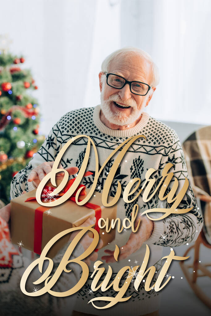happy senior man receiving christmas gift from wife near merry and bright lettering at home - Photo, Image