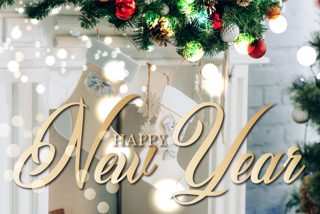 rama de pino decorado con medias de Navidad cerca de la chimenea y feliz año nuevo letras en casa - Foto, imagen