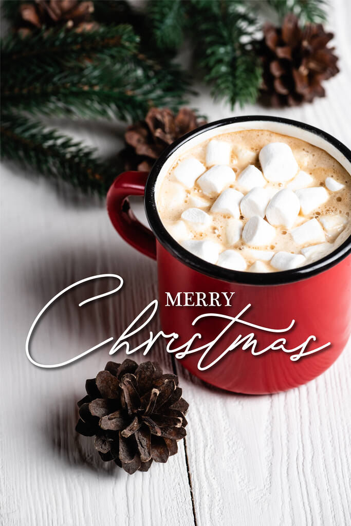 red cup of cocoa near pine cone and merry christmas lettering on blurred wooden background - Photo, Image