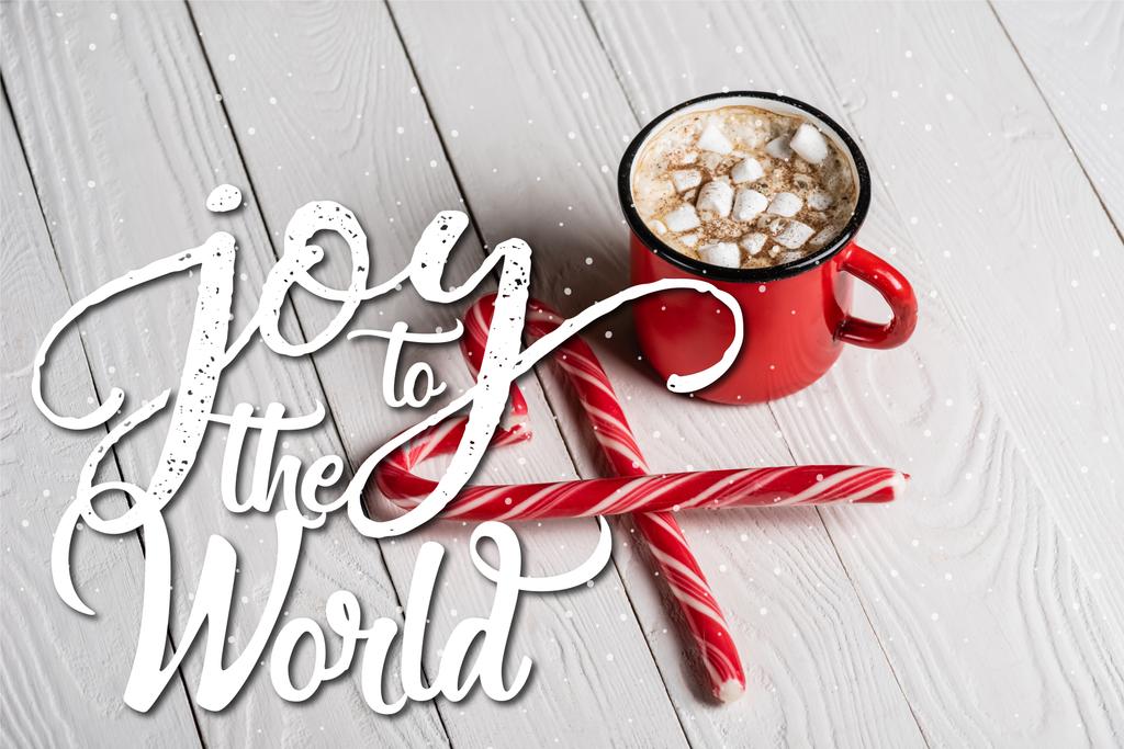 Червона чашка какао поблизу різдвяних цукерок біля радості всьому світу, що розкладається на дерев'яному фоні
 - Фото, зображення